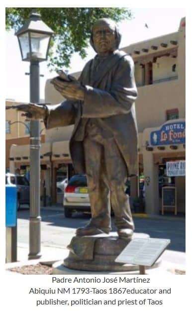 A bronze statue of Padre Antonio José Martínez stands in a plaza near Hotel La Fonda, featuring traditional Southwestern architecture.